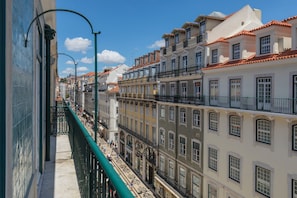 Une rue étroite, bordée de bâtiments des deux côtés, avec des balcons et une rambarde métallique verte.