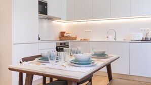 Una cocina moderna con armarios blancos, horno empotrado y comedor con mesa para cuatro.