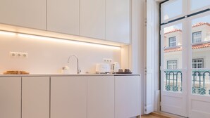 Una cocina moderna con armarios blancos, horno empotrado y ventana con vistas a un balcón con barandilla.