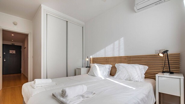 A neatly made bed with white linens and towels, a bedside table with a lamp, and a wooden headboard. - Downtown apartment w/terrace (Lisboa)