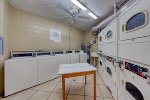 Un lavadero con varias lavadoras y secadoras, un ventilador de techo y una mesa.