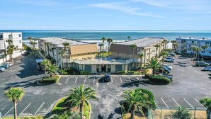 A hotel with a parking lot, palm trees, and a view of the beach. - Ocean view from every angle, Walkout property steps to the beach, Sunsets Galore (St. Augustine)
