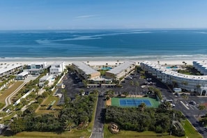 Un hotel frente al mar con varias construcciones, una playa y una cancha de tenis.