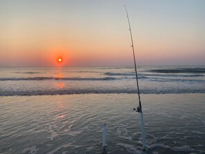 A fishing rod on a sandy beach with the sun setting in the background. - Ocean view from every angle, Walkout property steps to the beach, Sunsets Galore (St. Augustine)