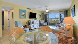 A living room with a glass table, wicker chairs, a sofa, a ceiling fan, and a view through the glass door. - Ocean view from every angle, Walkout property steps to the beach, Sunsets Galore (St. Augustine)