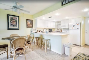 Cocina con armarios blancos, una isla central con taburetes, un ventilador de techo y un bote de basura.