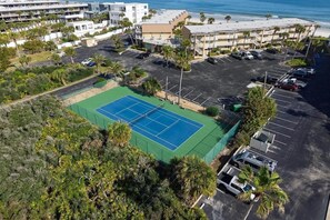 Vista aérea de un hotel con cancha de tenis, estacionamiento y vista al océano.