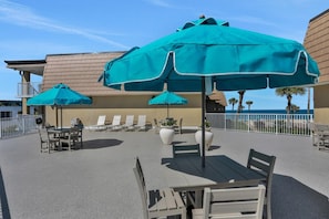 An outdoor seating area with tables and chairs, umbrellas, and a view of the ocean. - Ocean view from every angle, Walkout property steps to the beach, Sunsets Galore (St. Augustine)
