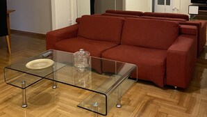 A living room with a red sofa, a glass coffee table, and a TV. - An elegant apartment in one of the most central areas of Athens. (Αθήνα)
