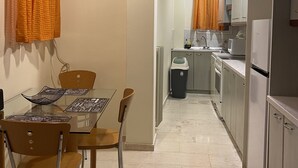 A compact kitchen with a dining area, featuring a glass table, chairs, and a trash bin. - An elegant apartment in one of the most central areas of Athens. (Αθήνα)