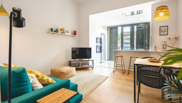 A modern living room with a teal sofa, a coffee table, a TV, and a dining area with stools. - Bravissimo Pont Areny, modern 3-bedroom apartment next to the historic center (Girona)