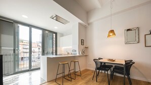 A modern kitchen with a central island, bar stools, and a dining area with a wooden table and chairs. - Bravissimo Pont Areny, modern 3-bedroom apartment next to the historic center (Girona)