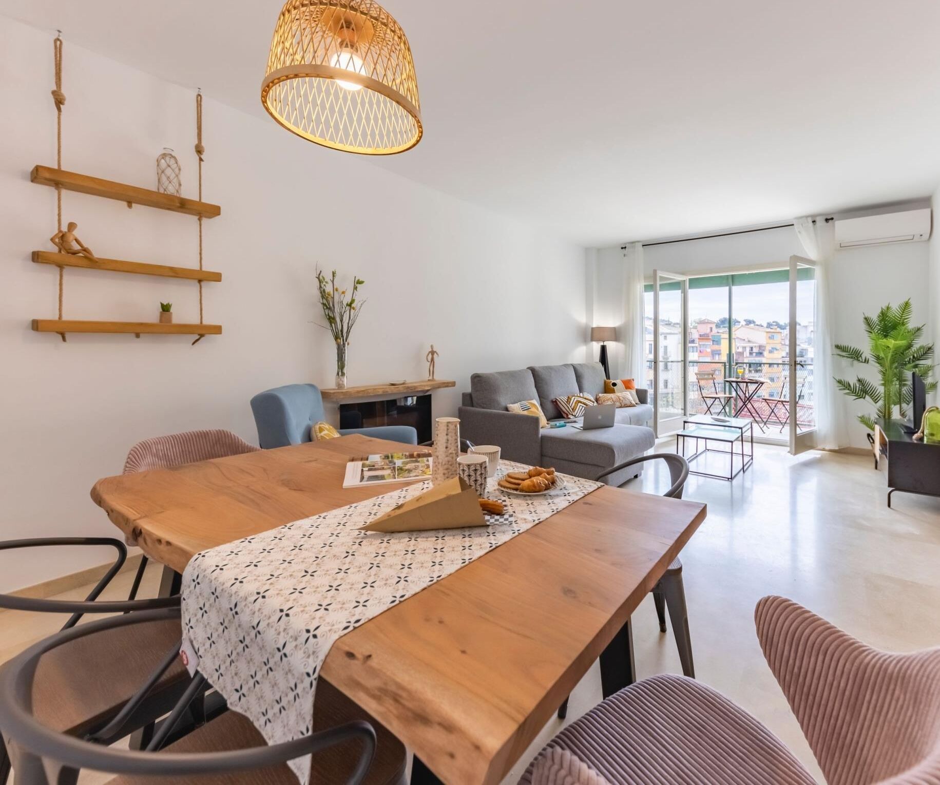 A modern living room with a wooden dining table, sofas, and a hanging light fixture.