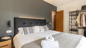 Un letto rifatto con una coperta grigia a righe bianche, un asciugamano bianco e una testiera nera.