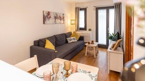 A modern living room with a grey sofa, a small table with a vase, and a painting on the wall. - Bravissimo Sant Martí; Cozy 1-bedroom apartment in Girona's historic center (Girona)