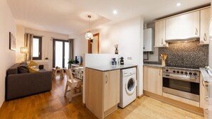 A compact apartment with a kitchenette, a washing machine, a dining area, and a living room with a sofa and a TV. - Bravissimo Sant Martí; Cozy 1-bedroom apartment in Girona's historic center (Girona)