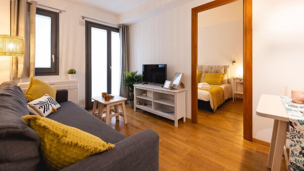 A modern living room with a grey sofa, a TV on a white stand, and a wooden floor. - Bravissimo Sant Martí; Cozy 1-bedroom apartment in Girona's historic center (Girona)