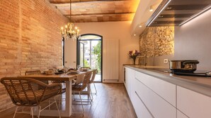 A modern kitchen with a brick wall, wooden dining table, wicker chairs, and a large window. - Bravissimo Plaça de la Independència, Garden View; High-quality luxury apartment (Girona)