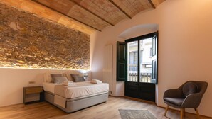 A bedroom with a stone wall, a bed, a chair, and a view of the outside. - Bravissimo Plaça de la Independència, Garden View; High-quality luxury apartment (Girona)