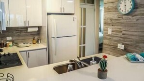 Una cucina moderna con mobili bianchi, un frigorifero, un lavello e una sveglia appesa al muro.