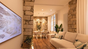 A cozy living room with a stone wall, a dining area with a table and chairs, and a large framed picture on the wall. - Bravissimo Ferreries, unique 3-bedroom apartment (Girona)