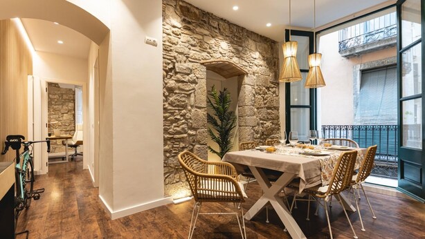 A dining area with a stone wall, wooden flooring, wicker chairs, and a table set for four. - Bravissimo Ferreries, unique 3-bedroom apartment (Girona)