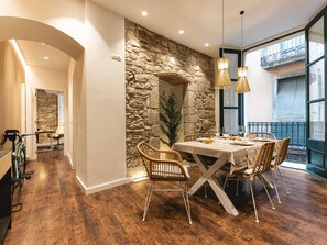 A dining area with a stone wall, wooden flooring, wicker chairs, and a table set for four. - Bravissimo Ferreries, unique 3-bedroom apartment (Girona)