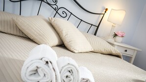 Cama bem arrumada com toalhas dobradas, abajur e um vaso com flores em uma mesa de cabeceira.