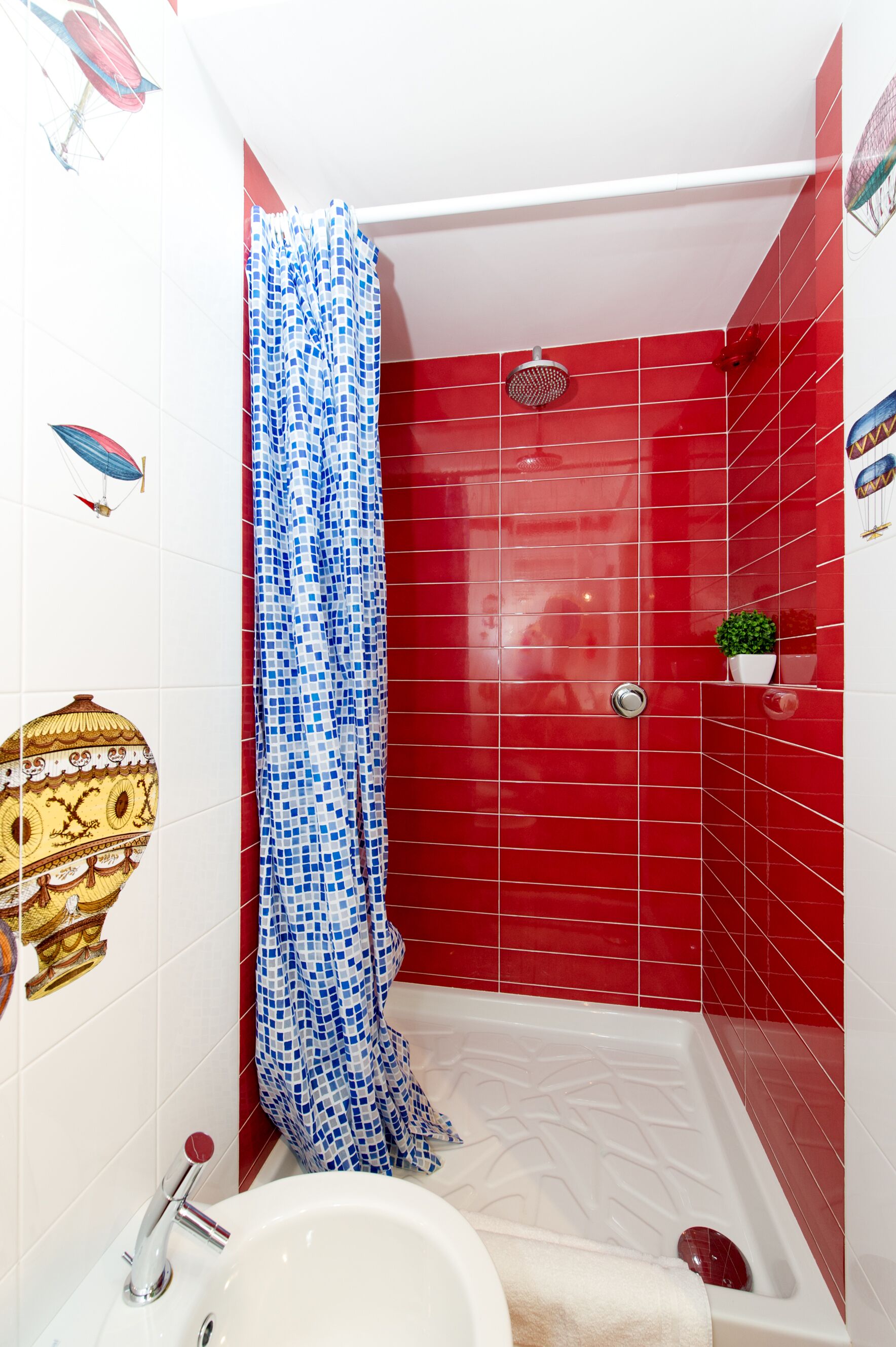 Une salle de bain avec des murs recouverts de carreaux rouges, une baignoire blanche, une douche dotée d’un rideau à motifs bleus et blancs, et un lavabo avec un robinet rouge.