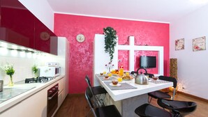 Cozinha moderna com parede vermelha de destaque, área de jantar com cadeiras e uma TV montada sobre o balcão.