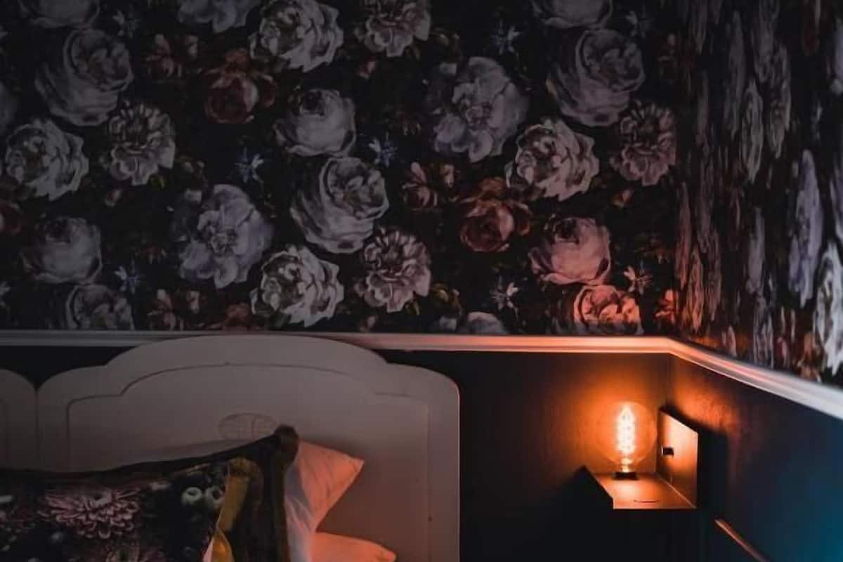 Cozy retreat with a comfortable bed and bedside table, set against a floral wallpaper backdrop.