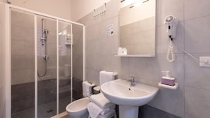 A modern bathroom with a glass shower enclosure, a pedestal sink, and a hairdryer mounted on the wall.