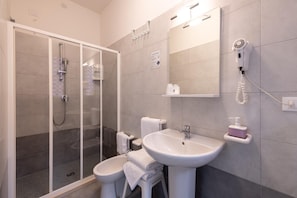 A modern bathroom with a glass shower enclosure, a pedestal sink, and a hairdryer mounted on the wall. - Anny Hotel (Jesolo)
