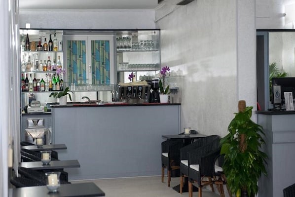 A modern bar area with a counter, shelves of liquor bottles, and a seating area with tables and chairs. - Anny Hotel (Jesolo)