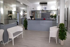 A modern reception area with a counter, seating, and a display of toiletries. - Anny Hotel (Jesolo)