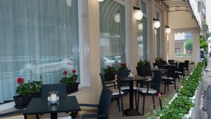 An outdoor cafe with tables and chairs, potted plants, and a view of the street.