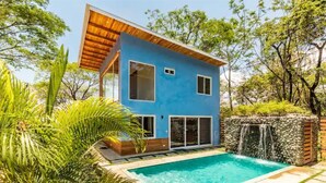 Een modern huis met twee verdiepingen, een blauwe gevel, een zwembad en een waterval.