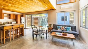 Une cuisine moderne avec un plafond en bois, un coin repas avec des chaises et une table, et un salon avec un canapé et une table basse.