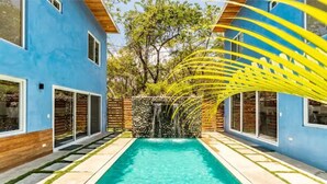 Un espace piscine moderne avec une piscine à l’eau d’un bleu limpide, entourée de murs bleus et d’une terrasse en bois.