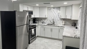 Eine moderne Küche mit weißen Schränken, einem schwarzen Kühlschrank, einer Marmor-Spritzschutzwand und einem Deckenventilator.