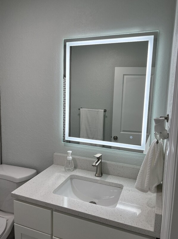 A modern bathroom with a large mirror, a white sink, and a toilet.