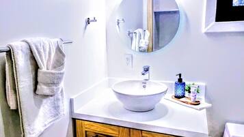 A bathroom with a round mirror, a white sink, wooden cabinets, and a towel rack.