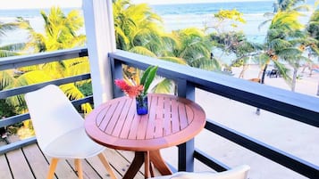 Eine Holzterrasse mit einem runden Tisch und zwei Stühlen, mit Blick auf einen Strand mit Palmen und dem Meer.
