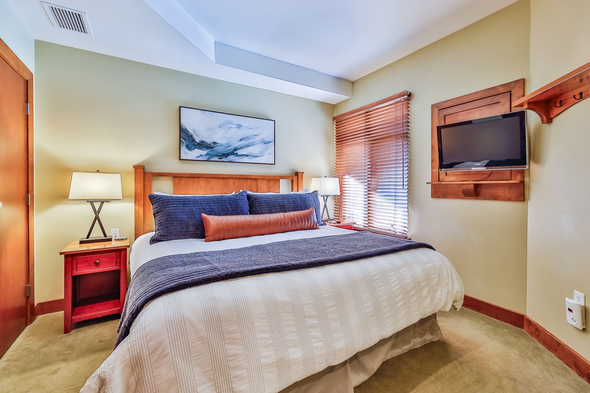 A hotel room with a large bed, two bedside tables with lamps, a mounted TV, and a ceiling light.