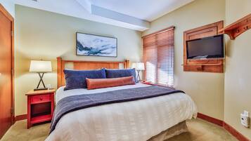 A hotel room with a large bed, two bedside tables with lamps, a mounted TV, and a ceiling light.