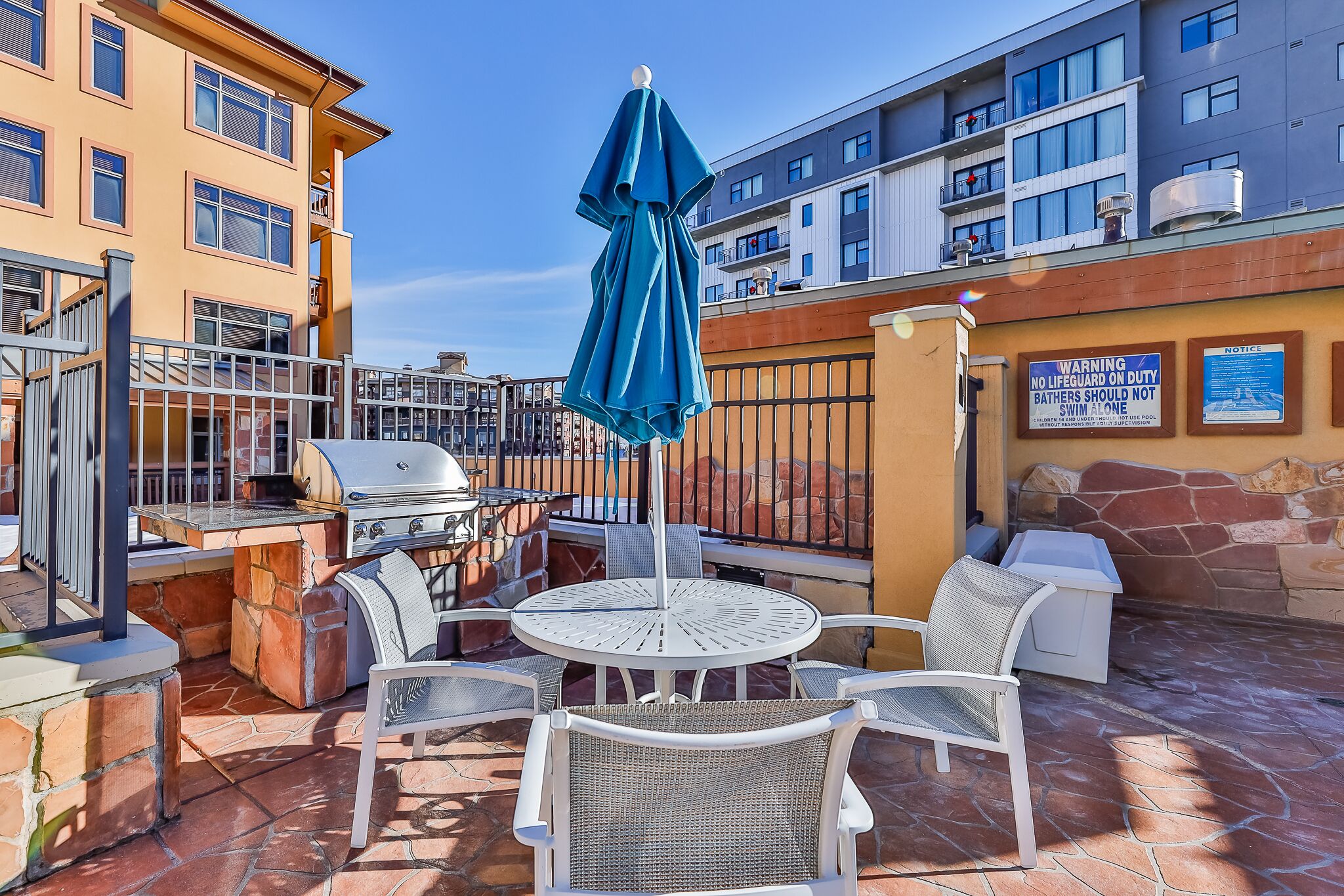 An outdoor patio with a grill, seating, and a blue umbrella.