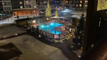 A heated outdoor pool area with a snow-covered landscape, surrounded by buildings with illuminated windows.