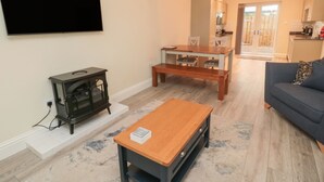 A living room with a TV, a coffee table, a sofa, and a dining area with chairs. - Bamburgh Dunes (Bamburgh)