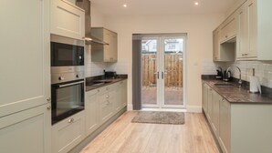 A modern kitchen with light-colored cabinets, a built-in oven, and a large window. - Bamburgh Dunes (Bamburgh)