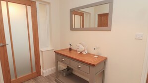 A bathroom with a wooden vanity, a mirror, and a small shelf with decorative items. - Bamburgh Dunes (Bamburgh)